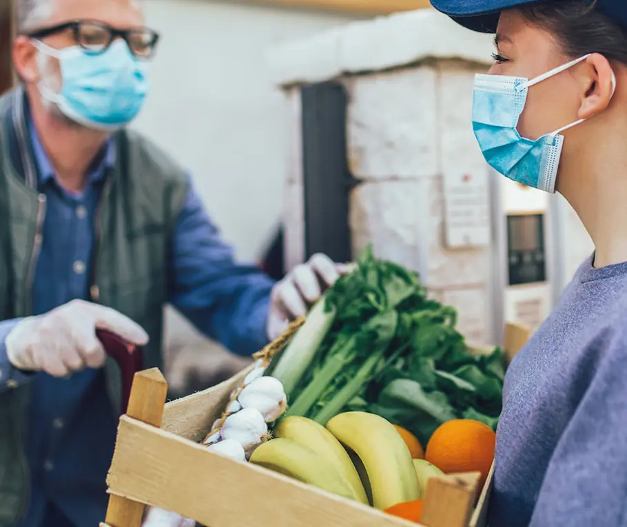 A man wearing masks and gloves holding a box of fruit.