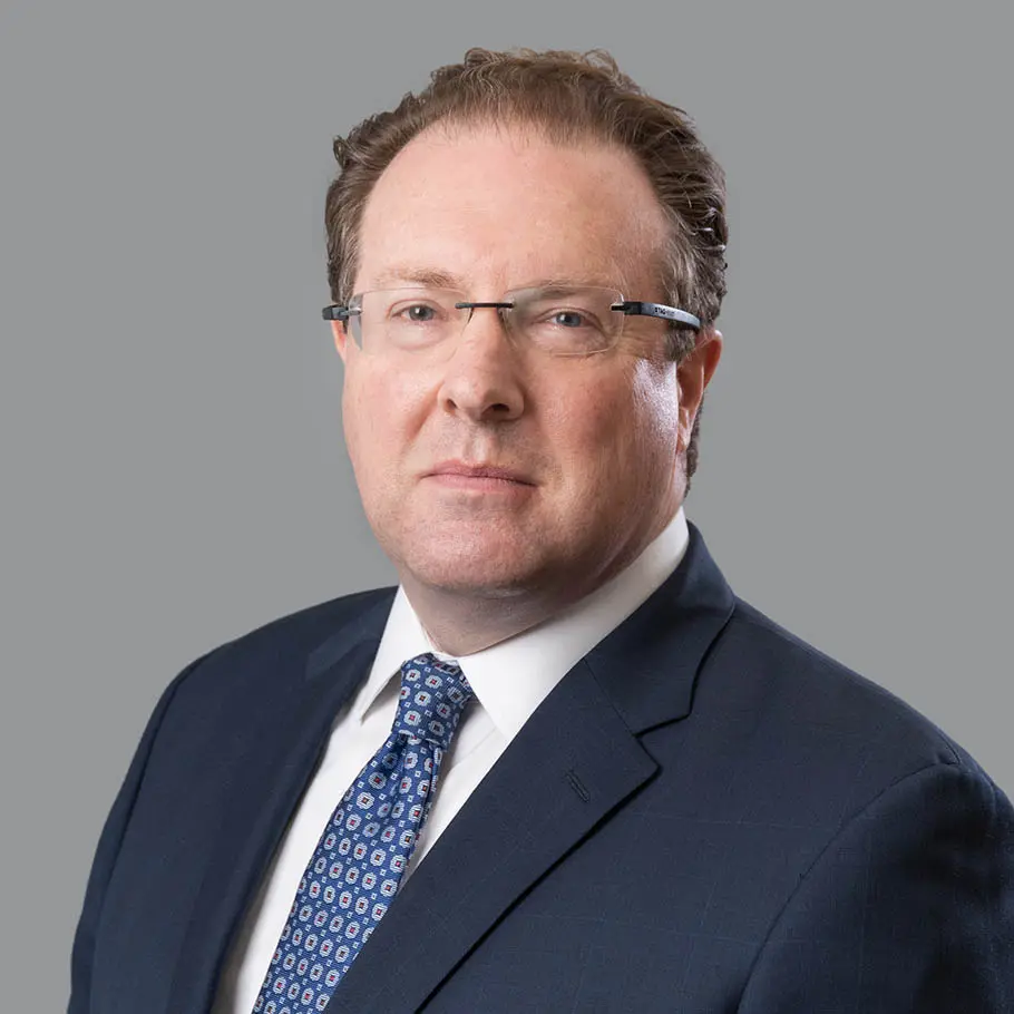 A man in a suit and tie standing up against a gray background.