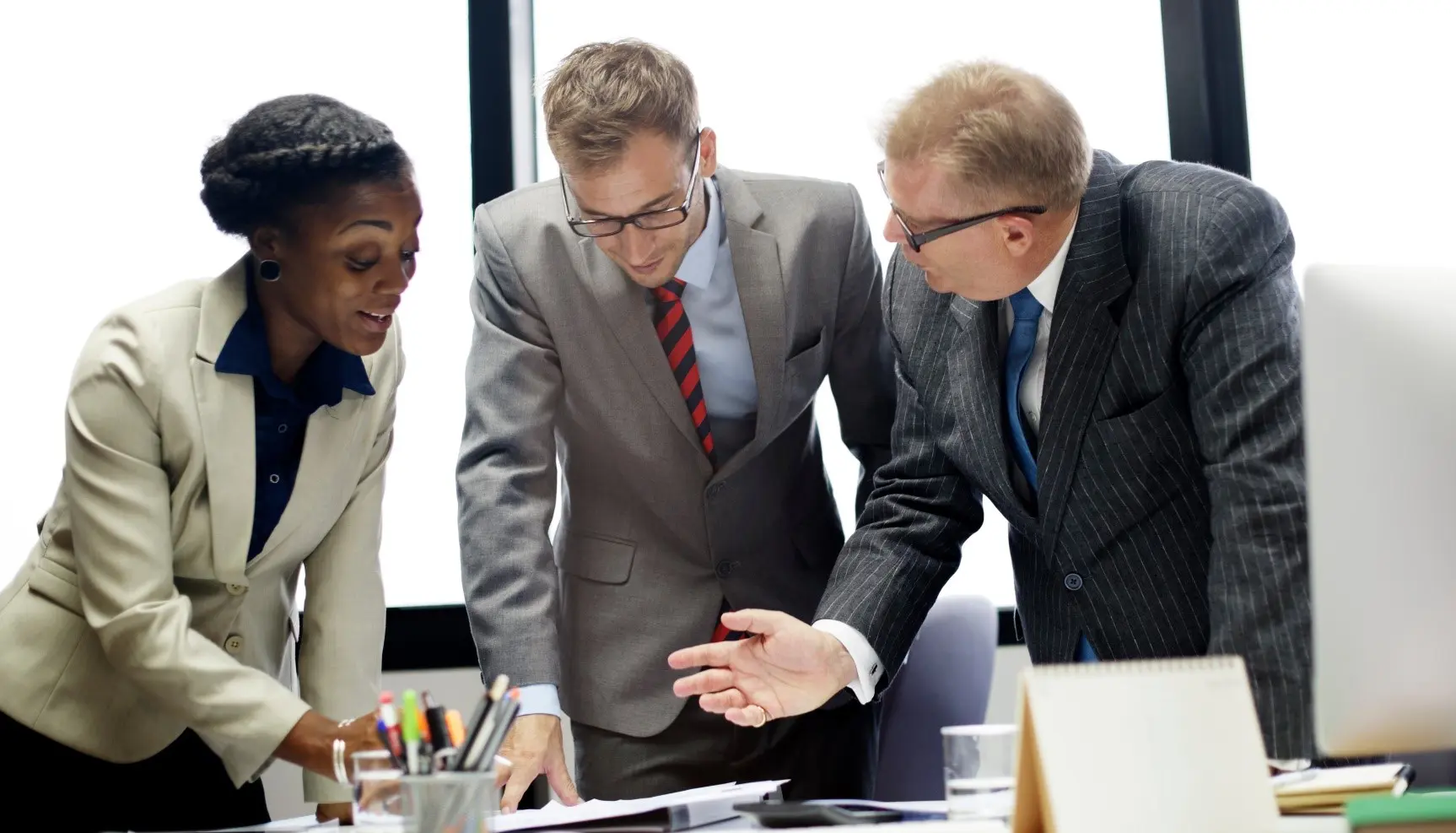 Three businesspeople discussing paperwork in office.