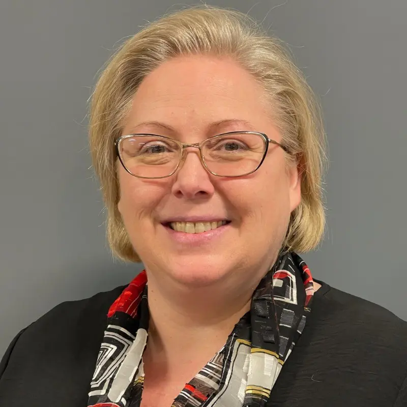 Woman with blonde hair wearing glasses and scarf.